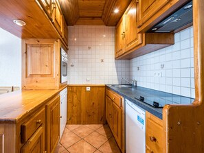 A kitchen with wooden cabinets, a white tiled backsplash, and a stainless steel sink.