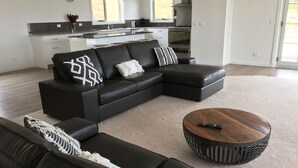 A modern living room with a sectional sofa, a round coffee table, and a kitchen in the background. - George River Park (Prestige House, 100 Acres, Animals, Bay/Mountain/Town Views) (St Helens)