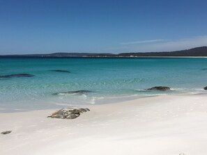A beach with clear turquoise water, white sand, and scattered rocks. - George River Park (Prestige House, 100 Acres, Animals, Bay/Mountain/Town Views) (St Helens)