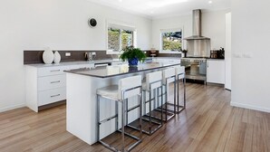 A modern kitchen with a central island, bar stools, a stove, and a large window. - George River Park (Prestige House, 100 Acres, Animals, Bay/Mountain/Town Views) (St Helens)
