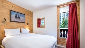 A bedroom with a bed, a wooden wall, a window with red curtains, and a balcony with a railing. - Renovated apartment in the heart of Val-d'Isère (Val-d'Isère)