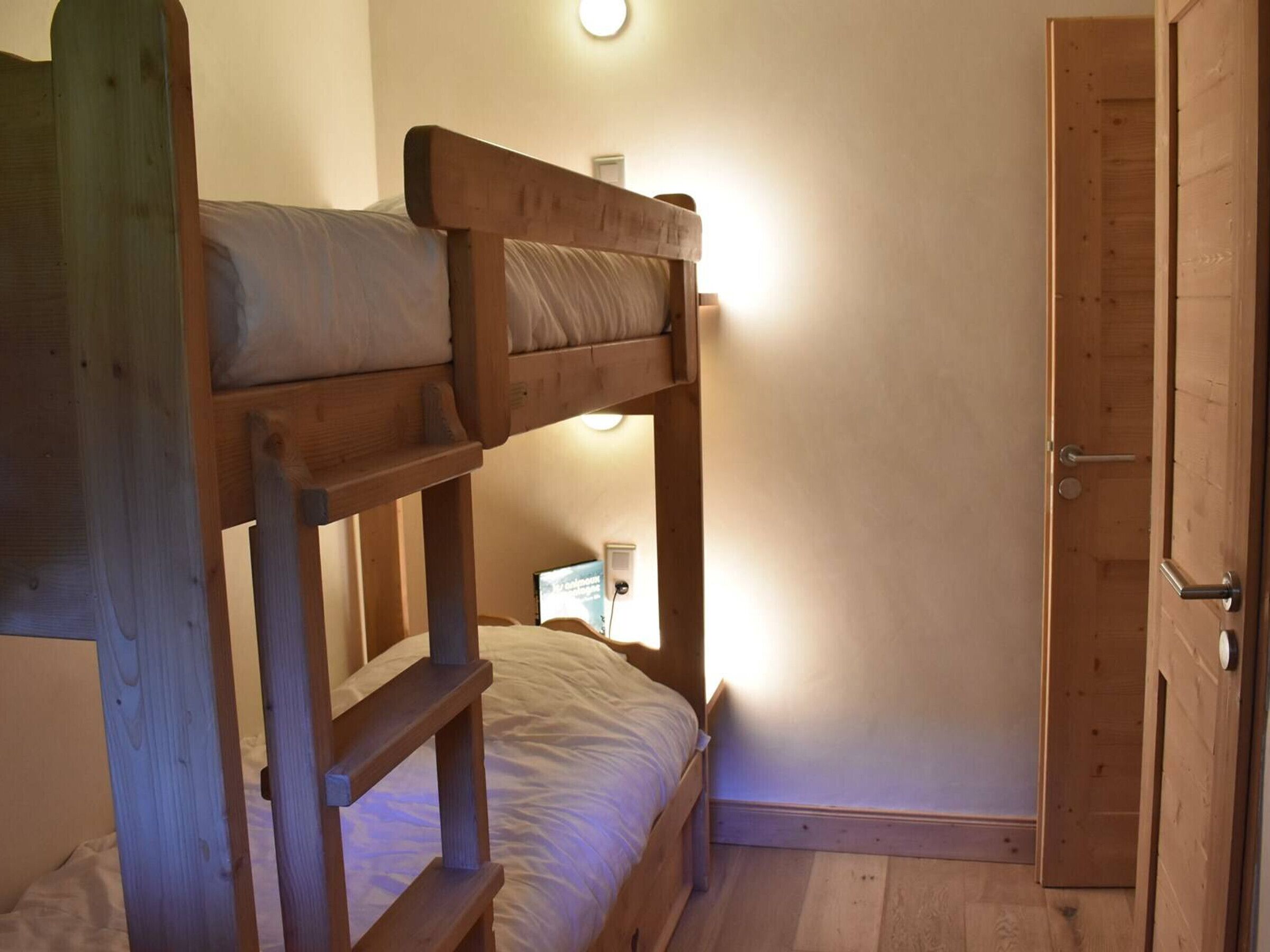 Ein kleines Zimmer mit Etagenbetten aus Holz, einem Nachttisch und einer Tür.
