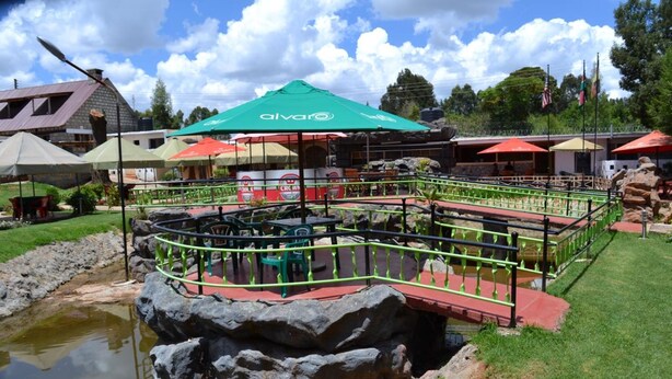 A restaurant with outdoor seating, a pond, and a rock formation. - Falls Hippo Point Hotel (Nyahururu)