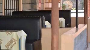 A restaurant interior with black cushioned booths, a tiled floor, and a stone wall. - Falls Hippo Point Hotel (Nyahururu)