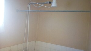 A bathroom with a shower, a towel rack, and a wall-mounted light fixture. - Falls Hippo Point Hotel (Nyahururu)