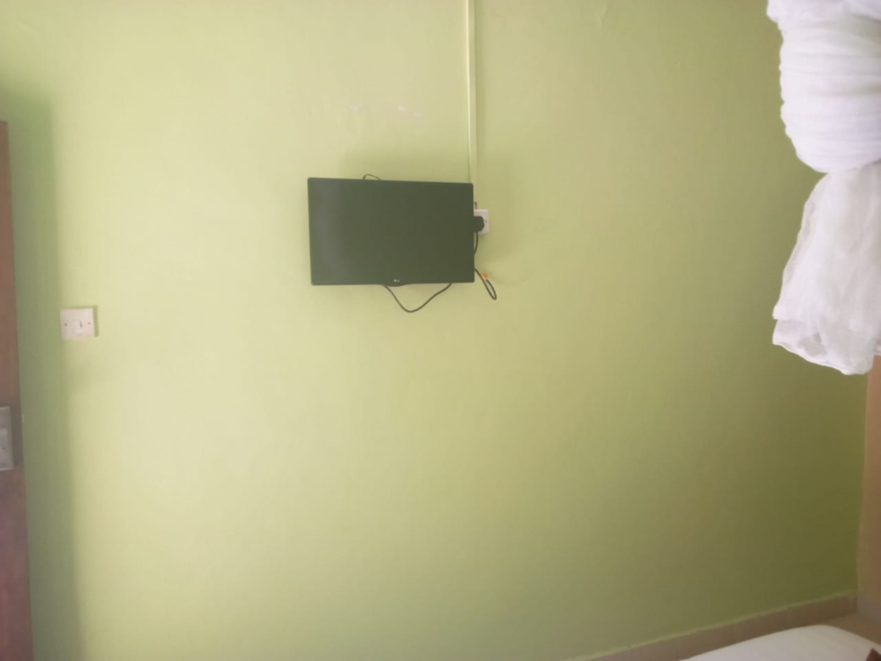 Ein Zimmer mit grüner Wand, einem daran befestigten schwarzen Stromkasten und einem weißen Vorhang auf der rechten Seite.