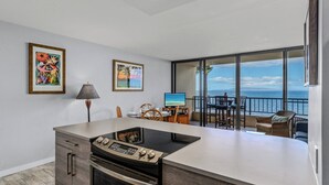 A modern kitchen with an island, a dining area with a view, and a balcony with a view of the ocean. - Sugar Beach PH31 Front Row Amazing Oceanviews in Highly Upgraded Unit (Kihei)