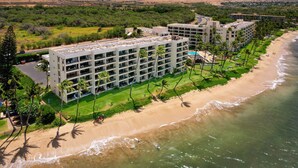 A beachfront hotel with multiple floors, a pool, and a beach area with palm trees. - Sugar Beach PH31 Front Row Amazing Oceanviews in Highly Upgraded Unit (Kihei)