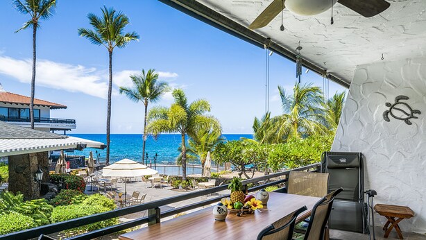 Ein Balkon mit Holztisch, Stühlen und Blick auf das Meer und Palmen.