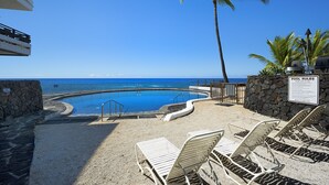 Ein Poolbereich mit Liegestühlen, einem Schild mit Poolregeln und Blick auf das Meer.