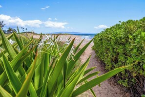 A pathway leading to a beach with a clear view of the ocean and distant mountains.