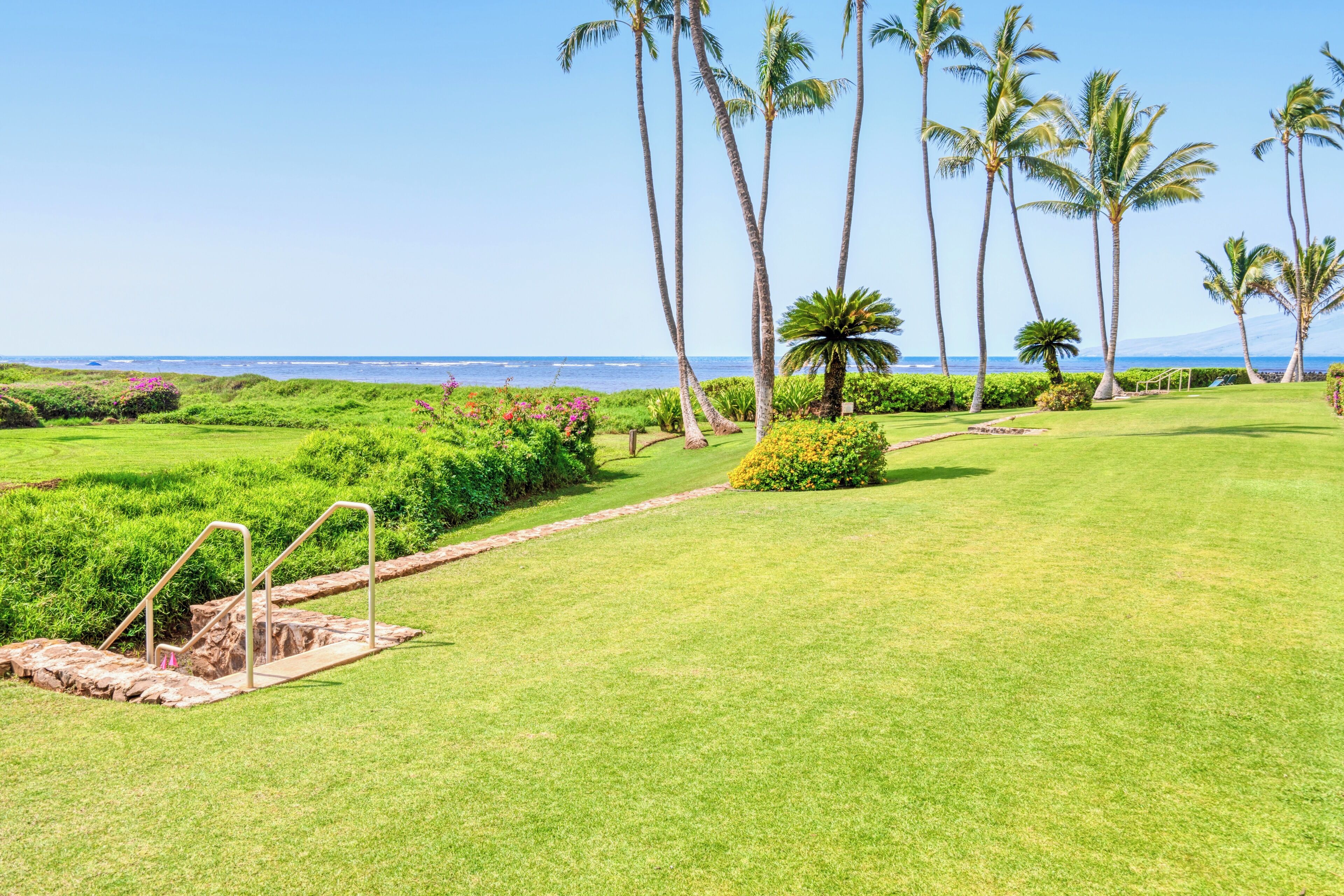 Ein gepflegter Golfplatz mit freiem Blick auf das Meer, Palmen und einem Steinweg, der zu einem Wasserspiel führt.