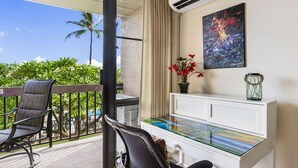 A balcony with a chair, a desk with a glass top, a potted plant, and a painting on the wall. - Maui Vista 3210 Wonderful unit With New Split AC, Low VO and New Paint and Carpet (Kihei)