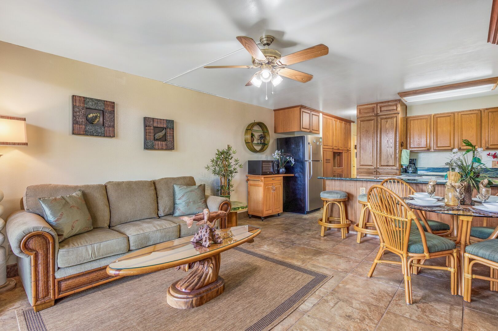 A spacious living area with a sofa, coffee table, and dining table with chairs. There is a kitchen with wooden cabinets and a refrigerator.