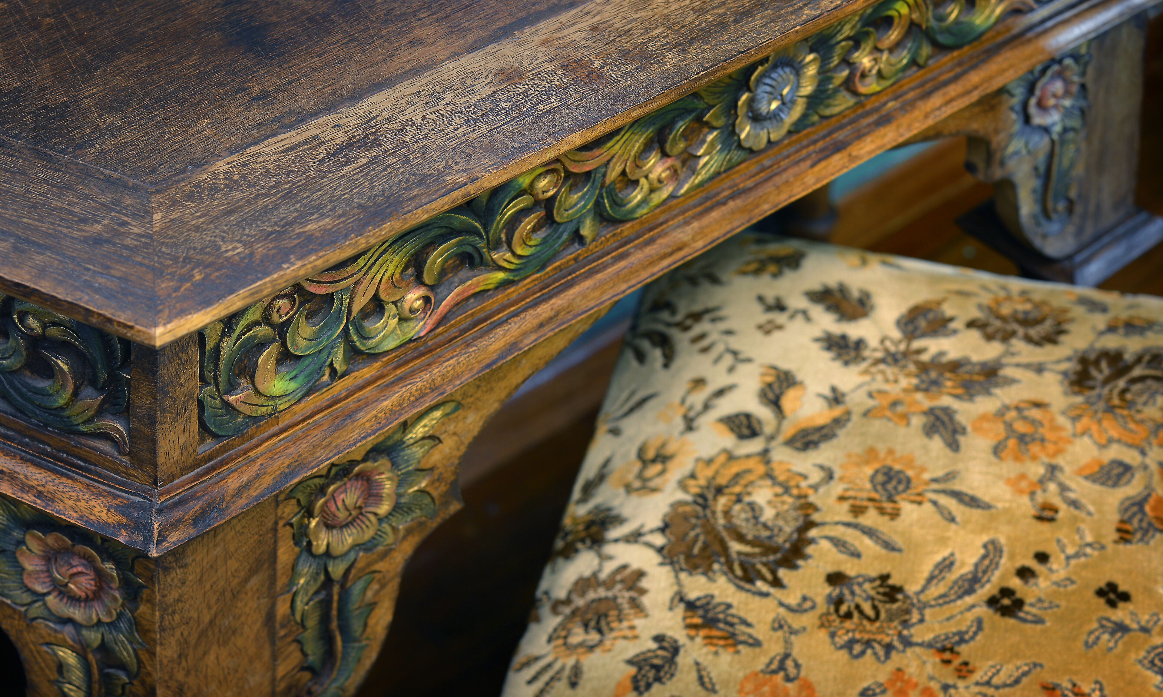 A wooden table with intricate carvings and a floral-patterned chair.