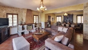 A spacious living room with a stone wall, a large sofa, a television, and a chandelier. - Infinity Villa Ioannina (Ioannina)