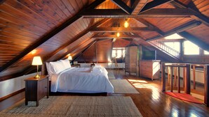 A high-ceilinged attic bedroom with a wooden floor, a bed, a nightstand, a desk, and a window. - Infinity Villa Ioannina (Ioannina)