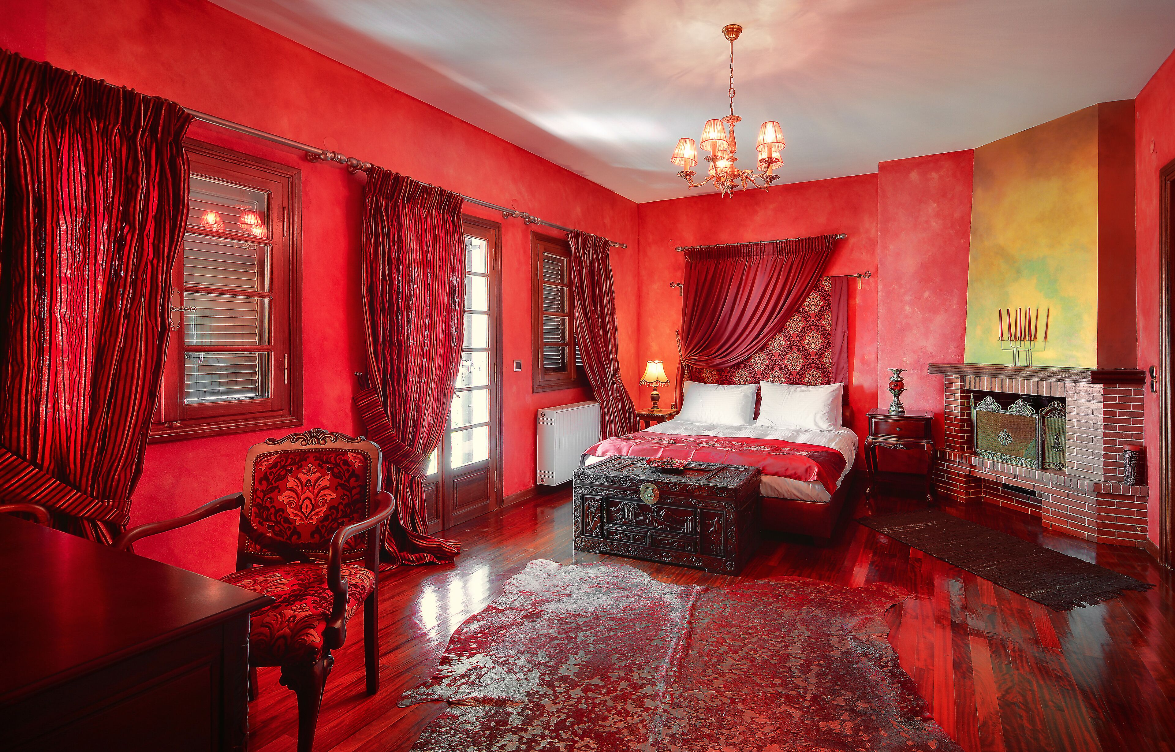 A room with a bed, a chair, a table, a fireplace, and curtains.