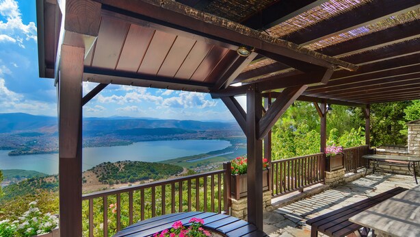 A wooden pergola with a stone bench and a table, overlooking a scenic lake and mountains. - Infinity Villa Ioannina (Ioannina)