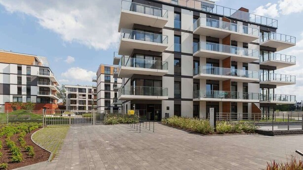 A multi-story residential building with balconies, a paved courtyard, and a small garden area.