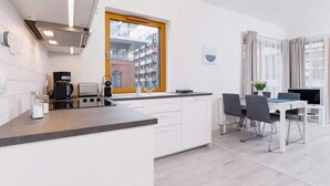 A modern kitchen with white cabinetry, a built-in stove, and a dining area with a table and chairs.