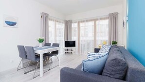 A modern living room with a grey sofa, a dining table with chairs, and a TV.