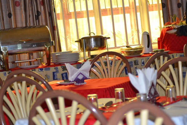A dining area with wooden chairs, a table set with plates, glasses, and a pot on a stand.