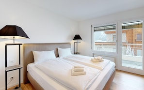 Habitación de hotel con una cama grande, dos lámparas de noche, vistas a un edificio a través de la ventana y suelo de madera.