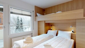 Ein Hotelzimmer mit Etagenbett, einem großen Fenster mit Blick auf schneebedeckte Bäume und einem hölzernen Kopfteil.