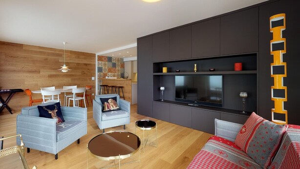 Ein modernes Wohnzimmer mit einer Couch, Sesseln, einem Couchtisch und einer TV-Wand.