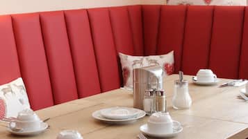 A dining table set with white tableware and a silver pitcher, surrounded by red upholstered seating.
