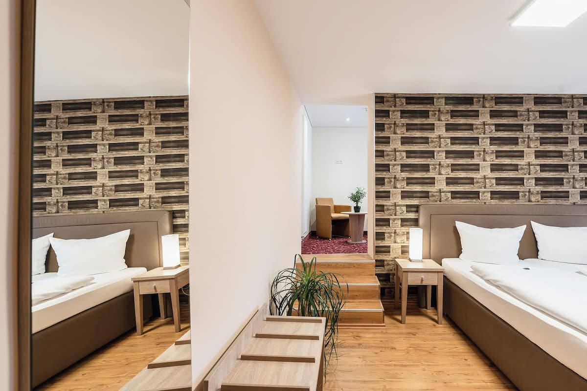 Una habitación de hotel moderna con dos camas, suelo de madera y pared con diseño de ladrillo.