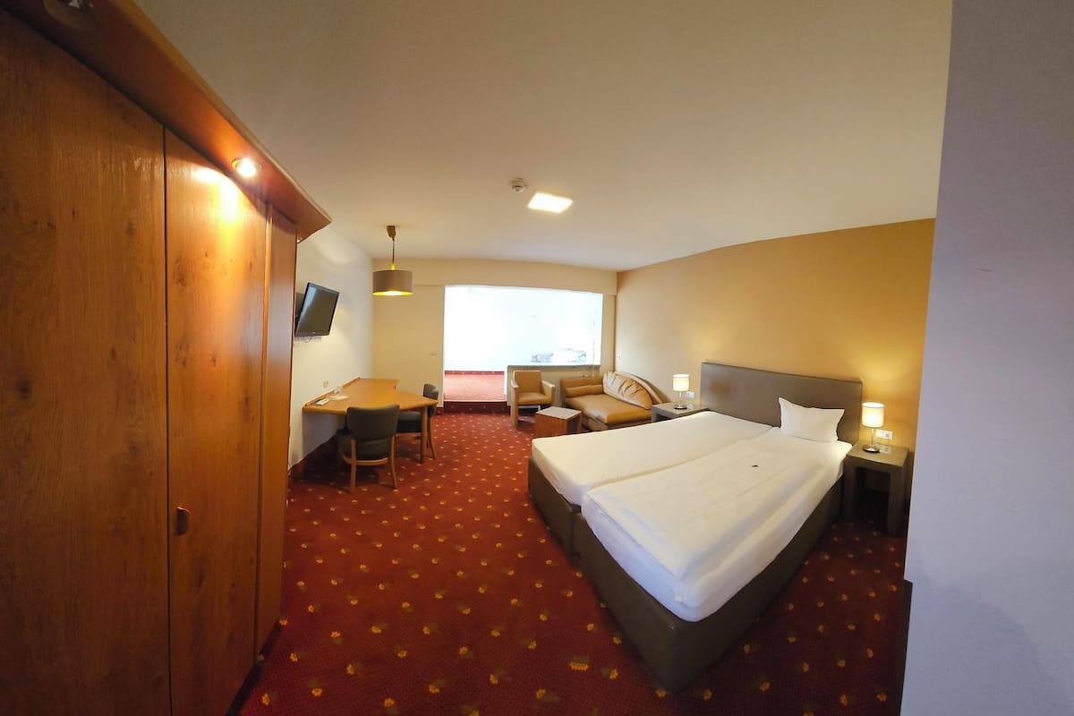 Una habitación de hotel con una cama grande, un escritorio, una silla, una mesita pequeña y un televisor.