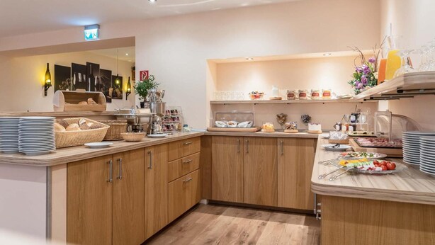Een moderne keuken met houten kastjes, een marmeren aanrechtblad en diverse ontbijtartikelen.