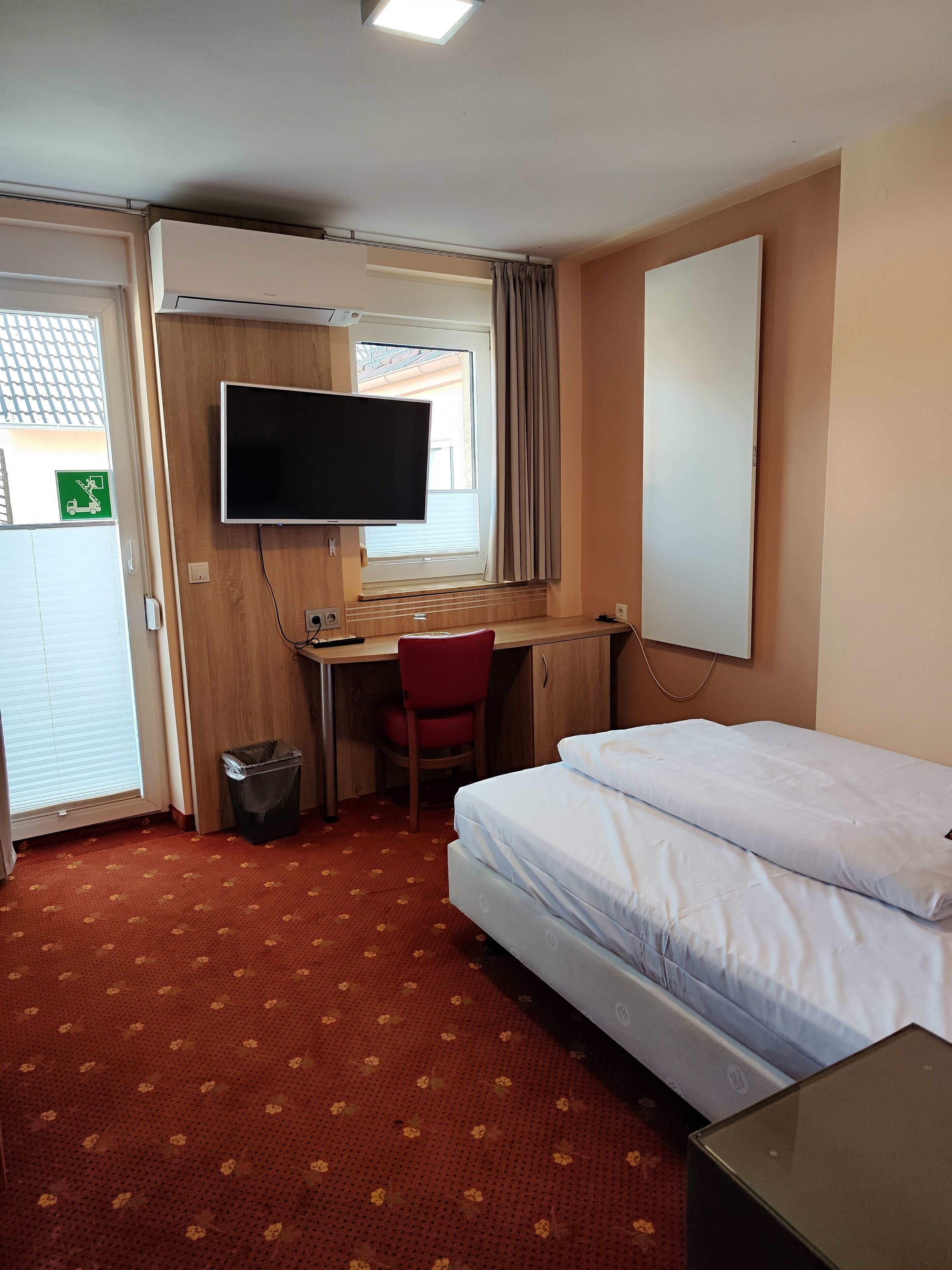 A hotel room with a bed, a desk, a chair, a TV, and a window with curtains.