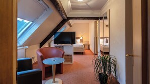 Een hotelkamer met een televisie, een bed, een tafeltje, een stoel, een potplant en een raam.