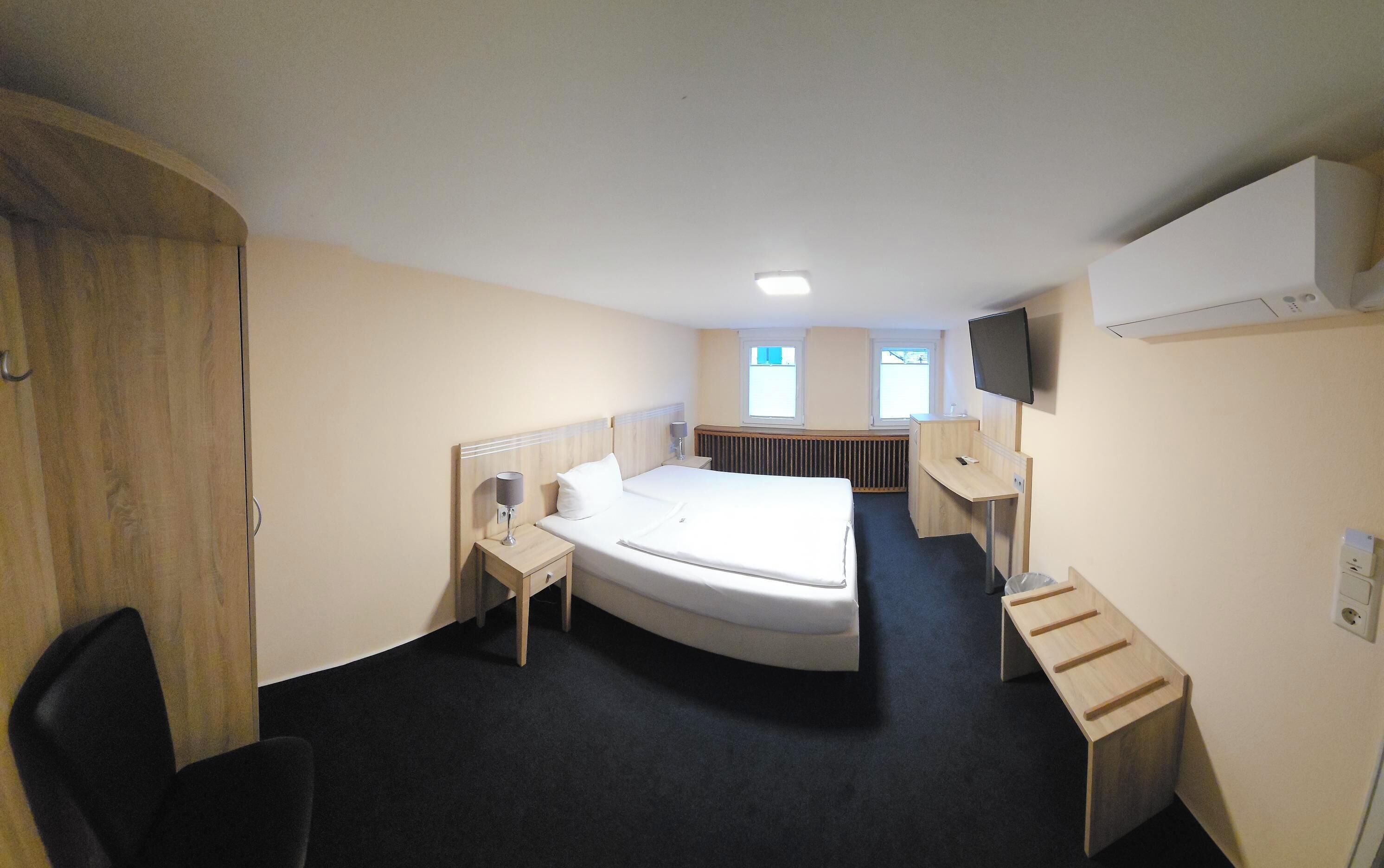 A compact hotel room with a single bed, a desk, a chair, a TV, and a window.