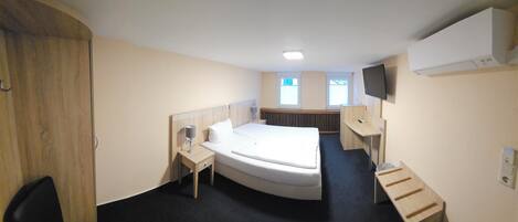 A compact hotel room with a single bed, a desk, a chair, a TV, and a window.