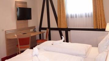 Una habitación de hotel con cama, escritorio, silla, televisor y ventana con cortinas.