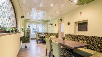 A dining area with a wooden table, green upholstered benches, and a patterned wall.