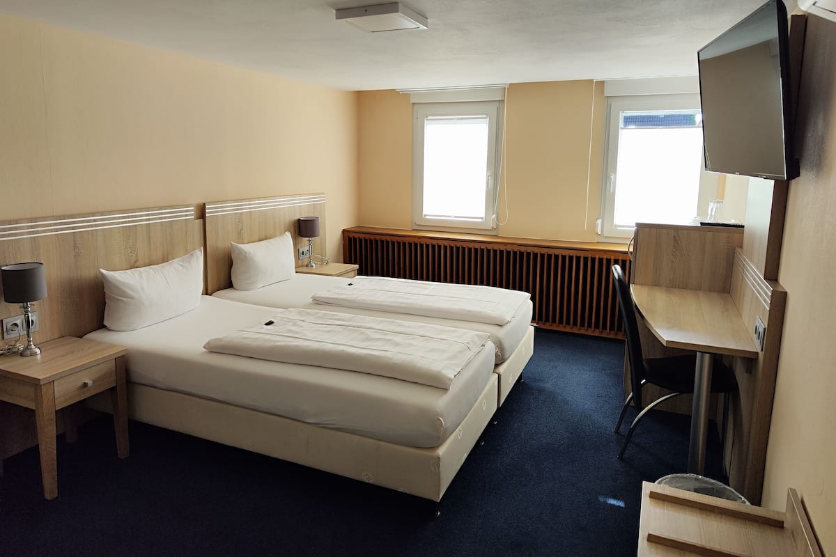 Una habitación de hotel con dos camas, un escritorio, una silla, un televisor y una ventana.