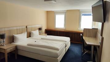 A hotel room with two beds, a desk, a chair, a TV, and a window.