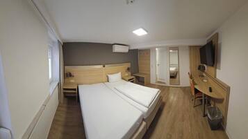 Habitación de hotel con una cama grande, un escritorio, una silla, un televisor y un espejo.