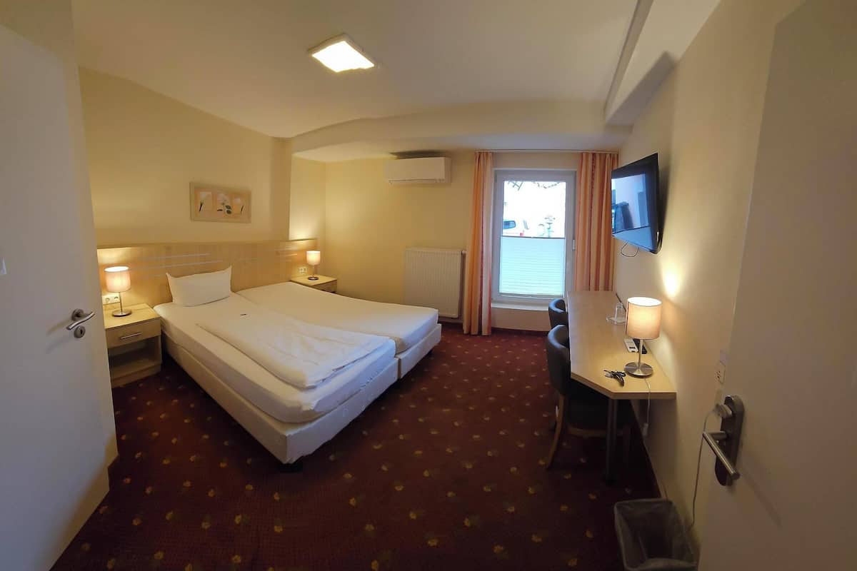 Una habitación de hotel con dos camas, un escritorio con silla, televisión y ventana con cortinas.