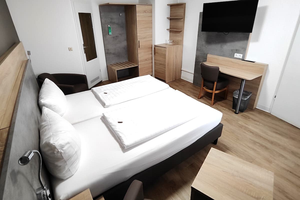 Habitación de hotel moderna con cama, escritorio, silla, televisión y almacenamiento integrado.