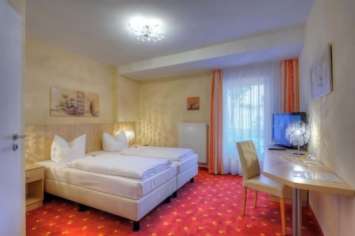 Habitación de hotel con dos camas, un escritorio, una silla, un televisor y una ventana con cortinas.