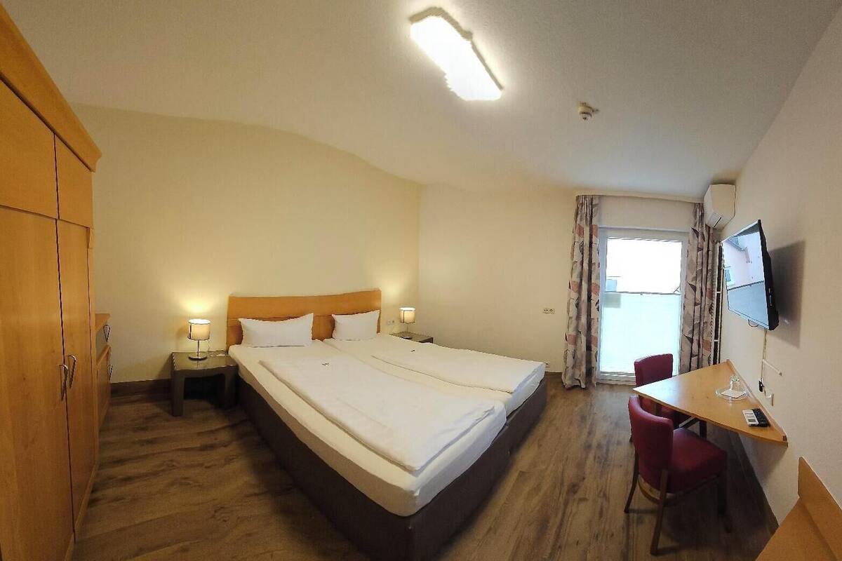 Habitación de hotel con una cama grande, un escritorio, una silla, un armario, un televisor y una ventana con cortinas.