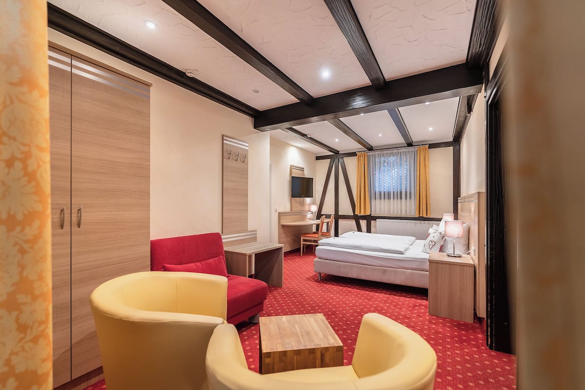 Habitación de hotel con cama, dos sillas, escritorio, armario y alfombra roja.