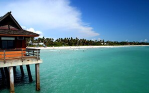 A wooden structure with a balcony overlooking turquoise waters and a beach with palm trees.