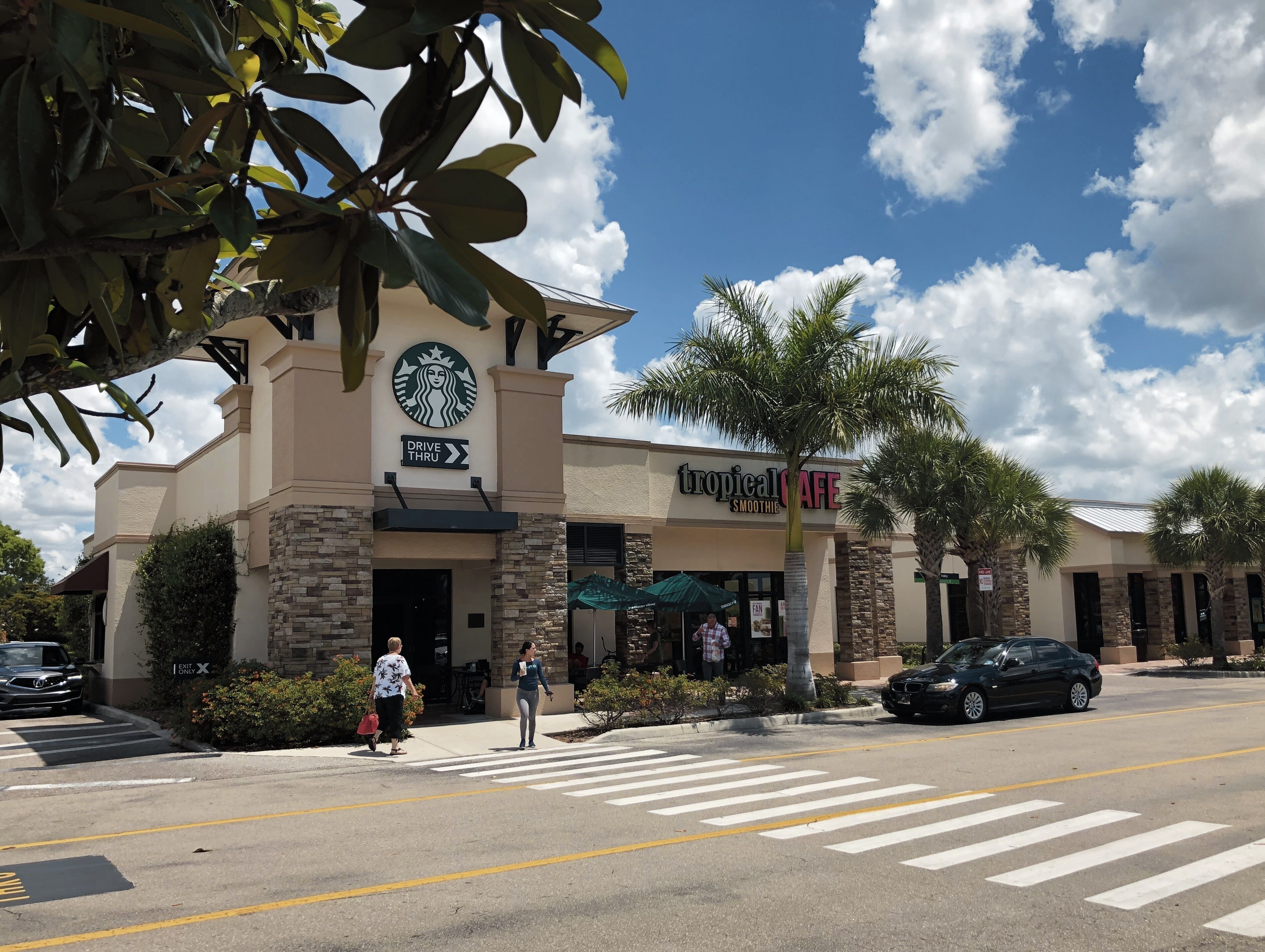 A Starbucks drive-thru and a Tropical Cafe with a crosswalk and palm trees.